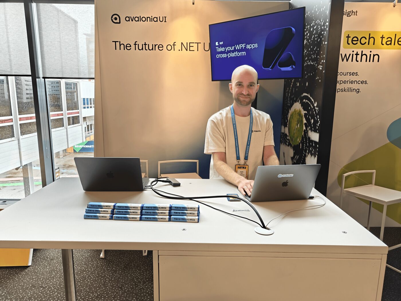 An Avalonia team member behind the booth desk at Techorama, under a screen showing Avalonia XPF