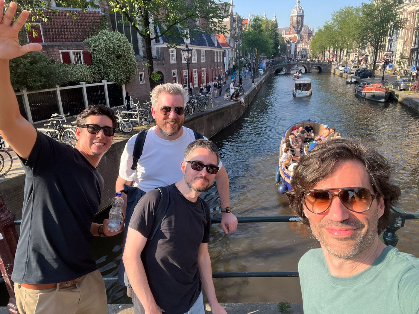 Four colleagues on a bridge over an Amsterdam canal, one of them waving at the camera
