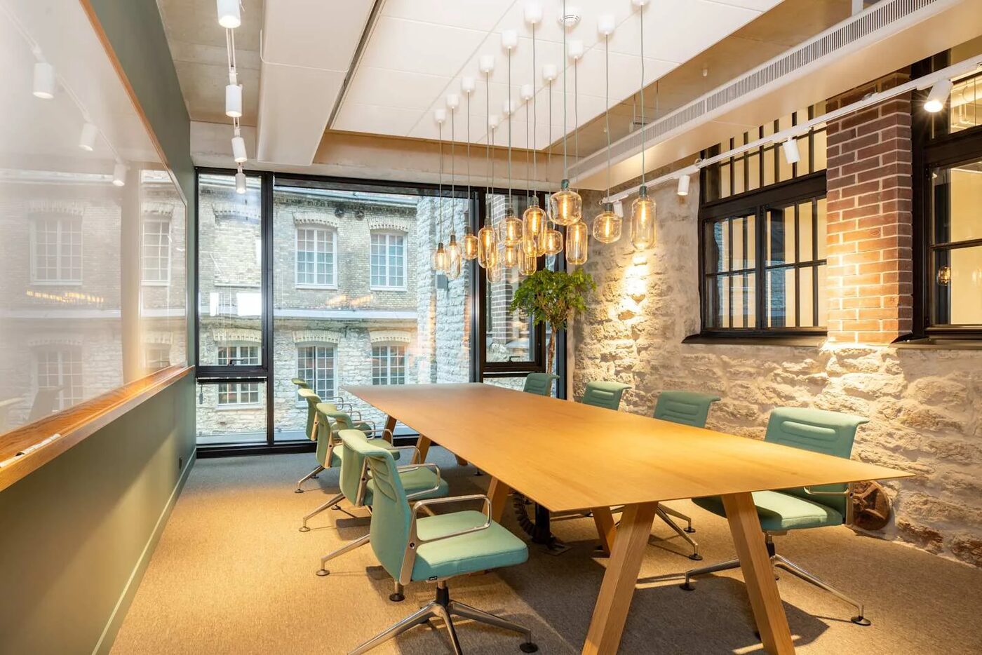 A meeting room in the Tallinn office with a long oak table, exposed limestone wall and pendant lights