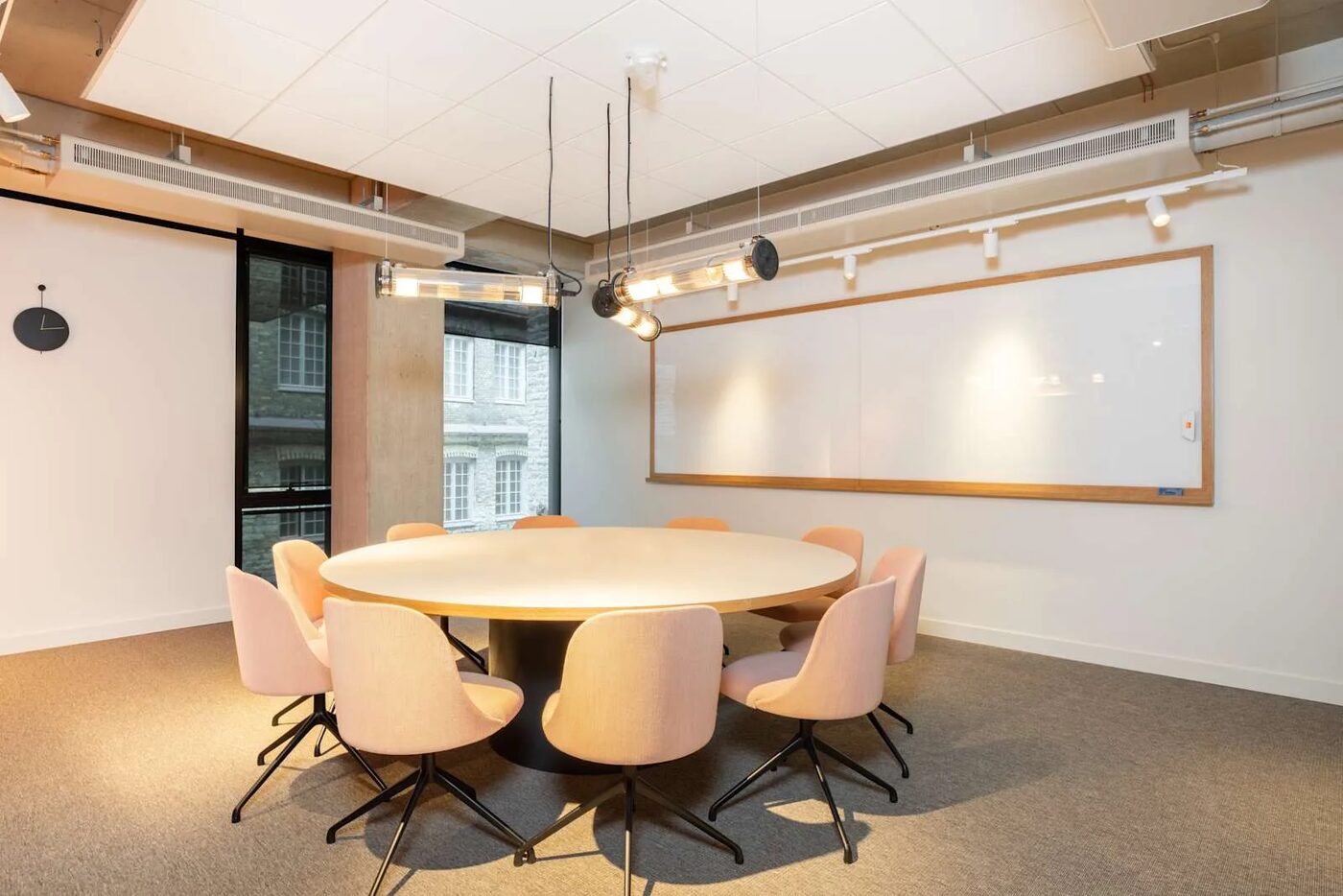 A round meeting table with pink chairs and a large whiteboard in the Tallinn office